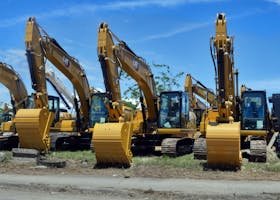 Multiple yellow excavators lined up in an equipment yard under a clear blue sky.